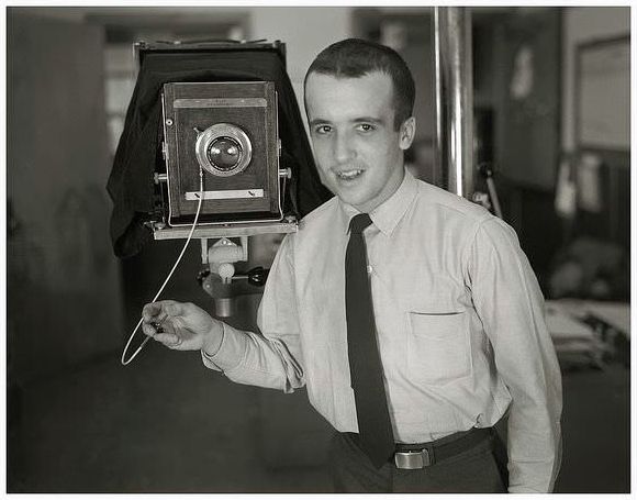 A young photographer poses with his Deardorff 10×8 camera attached to a studio stand.