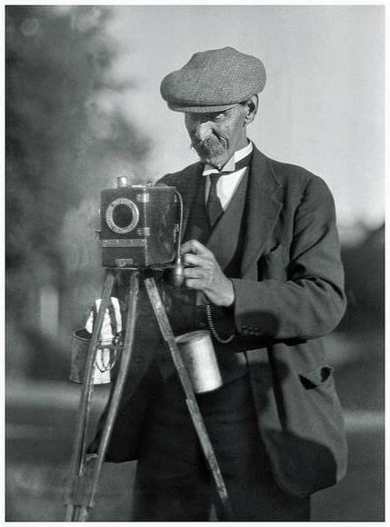A street photographer, somewhere in England, with his Moore &; Co Aptus Ferrotype camera. The processing solutions hang from the struts of his wooden tripod.