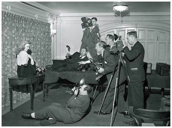 A group of Graflex wielding press photographers descend on a table bound model.