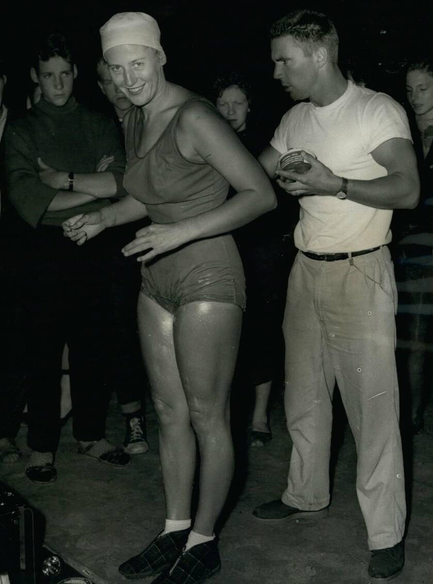 #21 Greta Anderson is greased by her husband P.T. Instructor John Sonnichsen before she entered the water to win the International Cross Channel Swimming race, 1958.