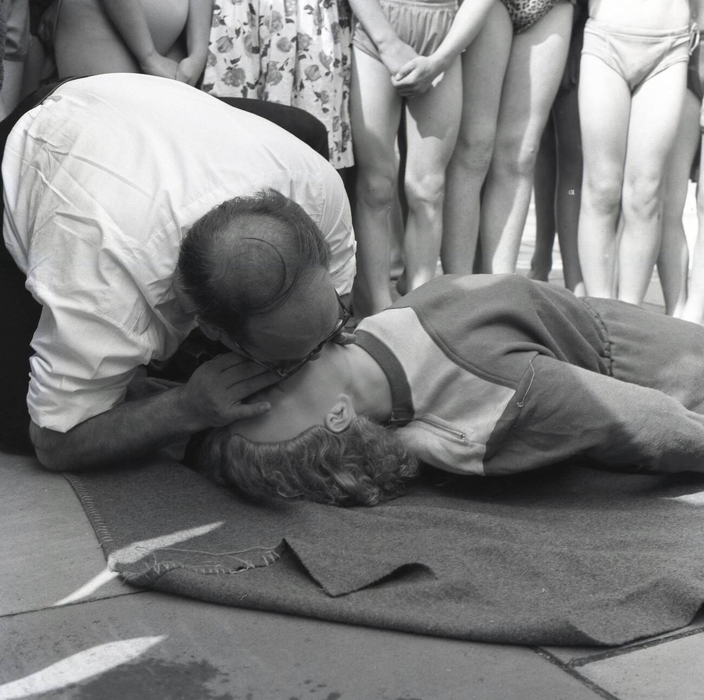 #22 An instructor demonstrates the ‘kiss of life’ to a training dummy as part of a life-saving demonstration for junior swimmers at Vale Pool, an open-air swimming pool in Aylesbury, Bucks, England, 1964.